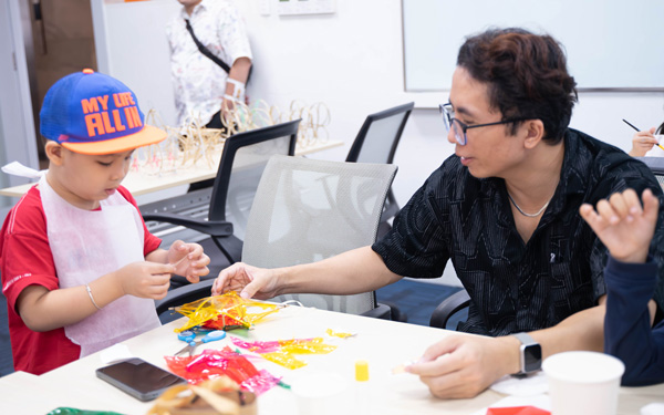 Người bố đang kiên nhẫn hỗ trợ con trai nhỏ hoàn thiện chi tiết trên chiếc lồng đèn.