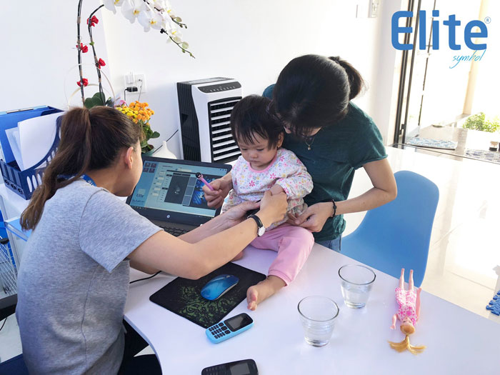 Chuyên viên Elite Symbol đang thao tác lấy dấu vân tay cho bé nhỏ có mẹ hỗ trợ